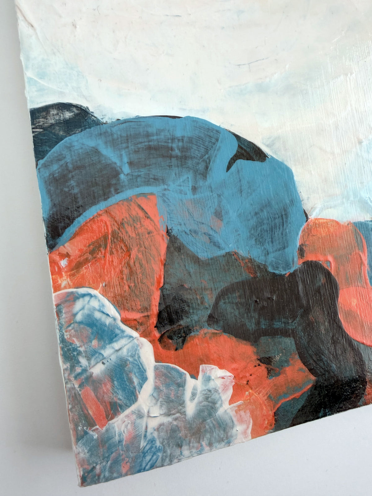 Abstract panel painting with thick textured brushstrokes in blue, orange, brown, and white, shown at an angle against a light background.