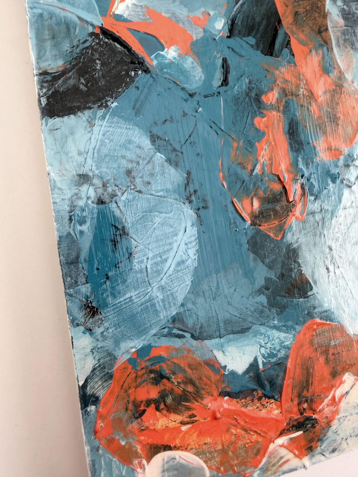 Abstract painting with thick textured brushstrokes in light blue, orange, brown, and white, shown close up against a neutral wall.