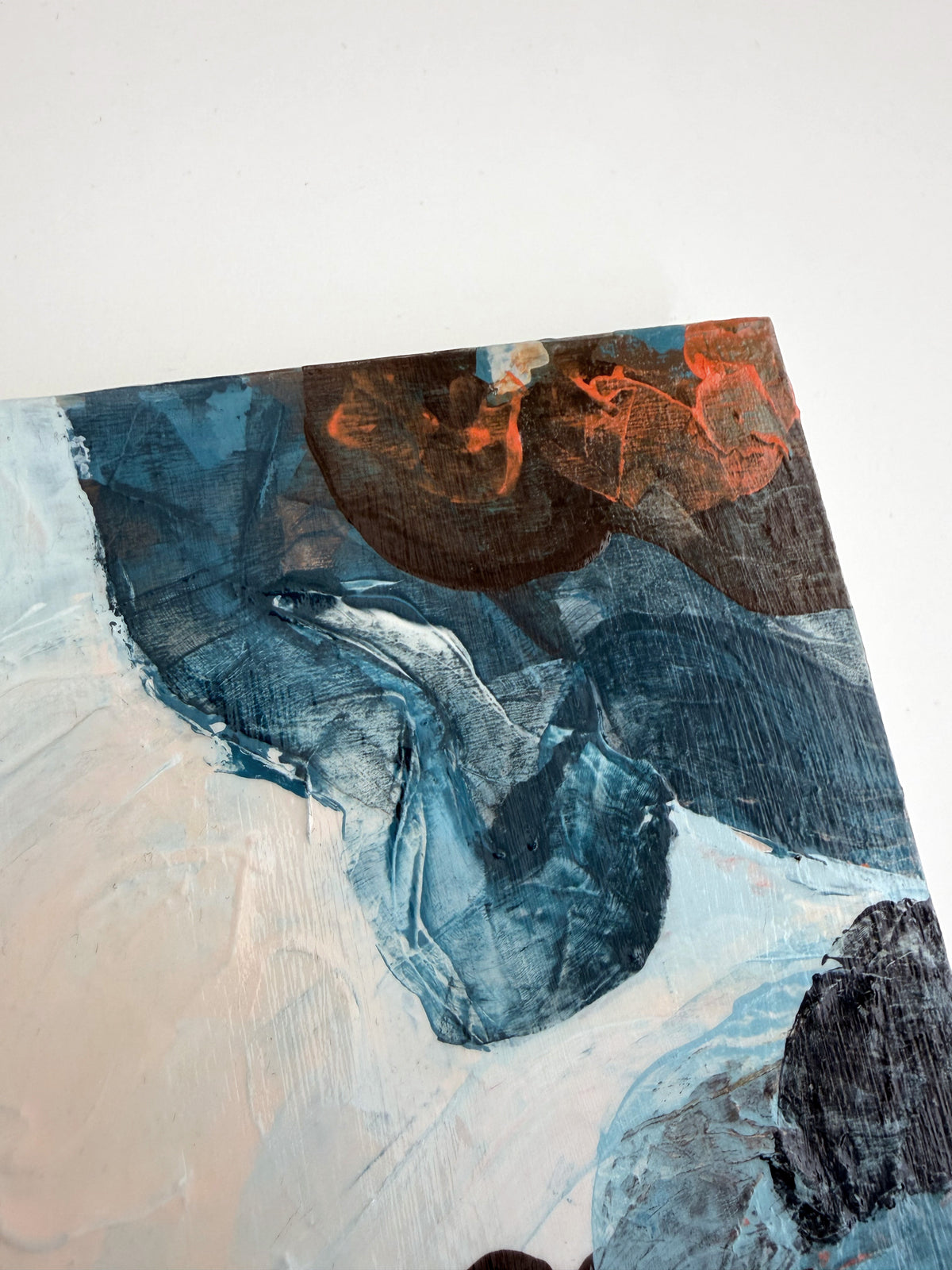 An abstract panel painting featuring textured impasto brushstrokes in deep blue, cream, and orange, shown at an angle against a plain white background.