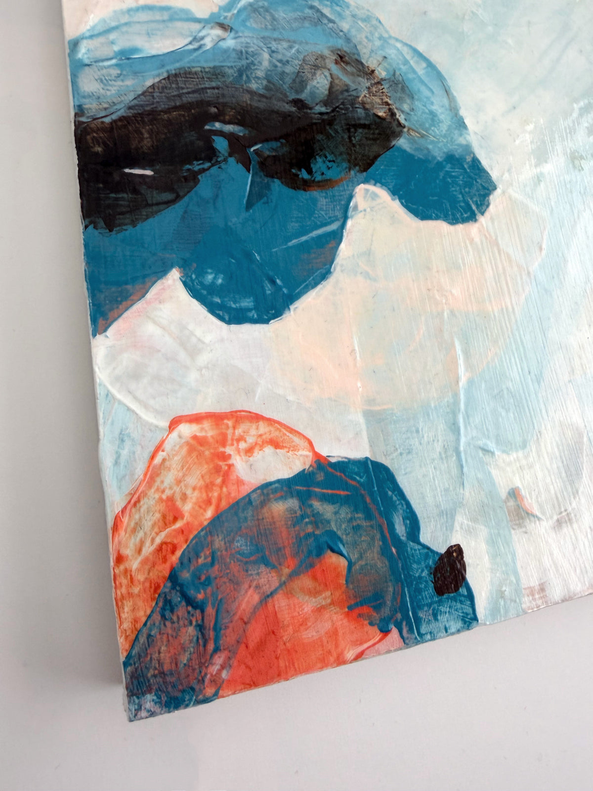 Abstract panel painting featuring textured brushstrokes in blue, white, orange, and brown, shown at an angle against a light wall.