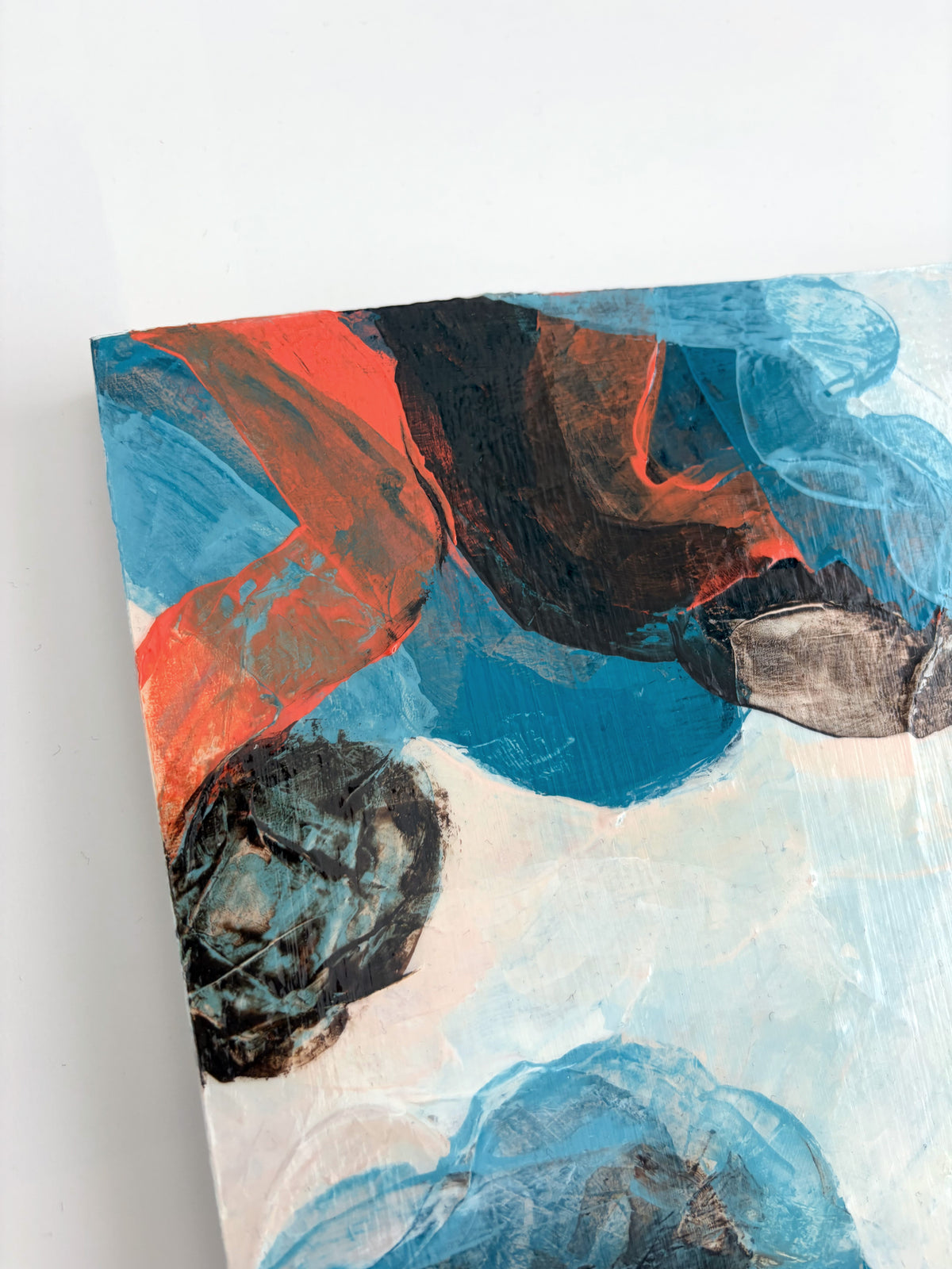 An abstract panel painting featuring expressive brushstrokes of blue, orange, brown, and white, shown angled against a plain white background.